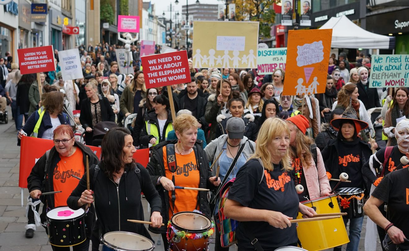 Image description: Women marching in the March of the Mummies protest with placards and drums