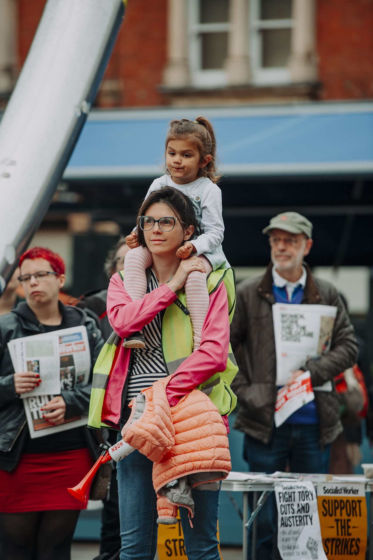 Alt text: Woman with child on her shoulders at the March of the Mummies protest