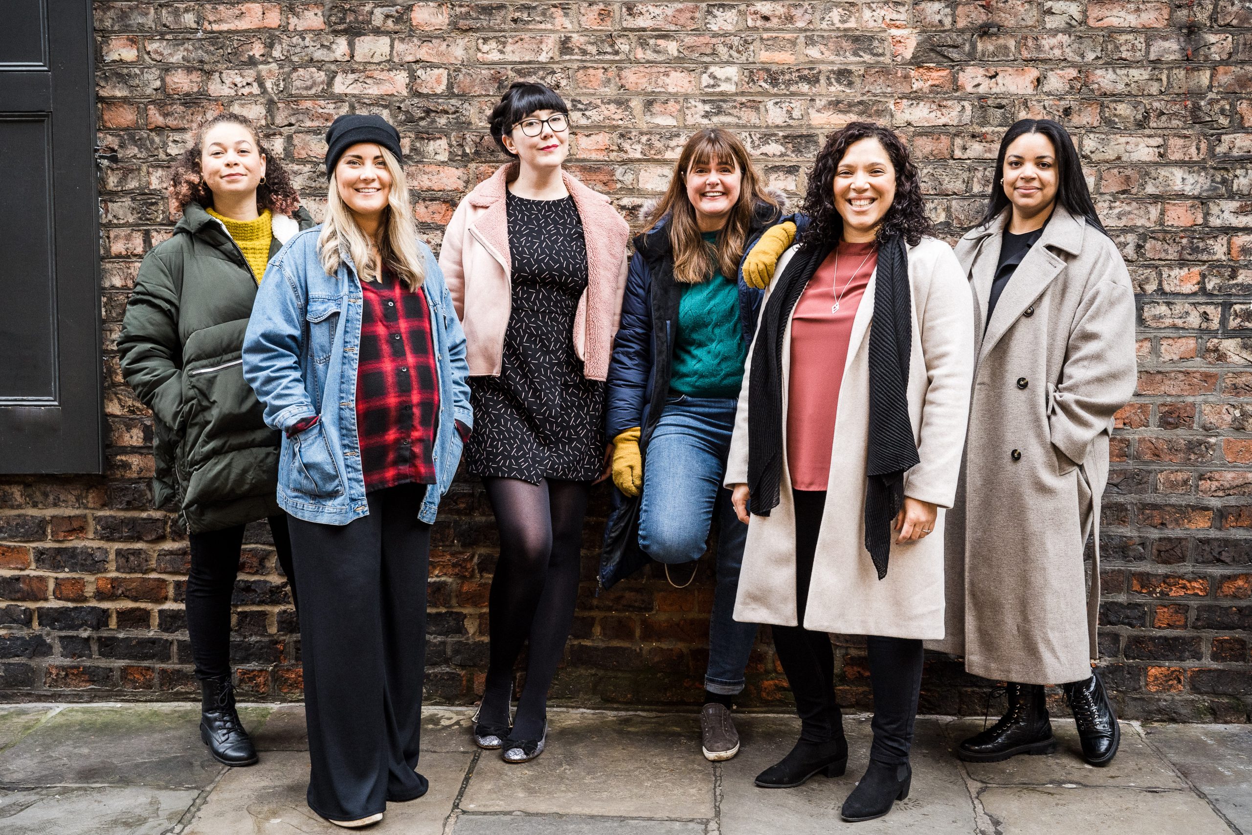 Alt text: The Pregnant Then Screwed team smiling together in front of a brick wall