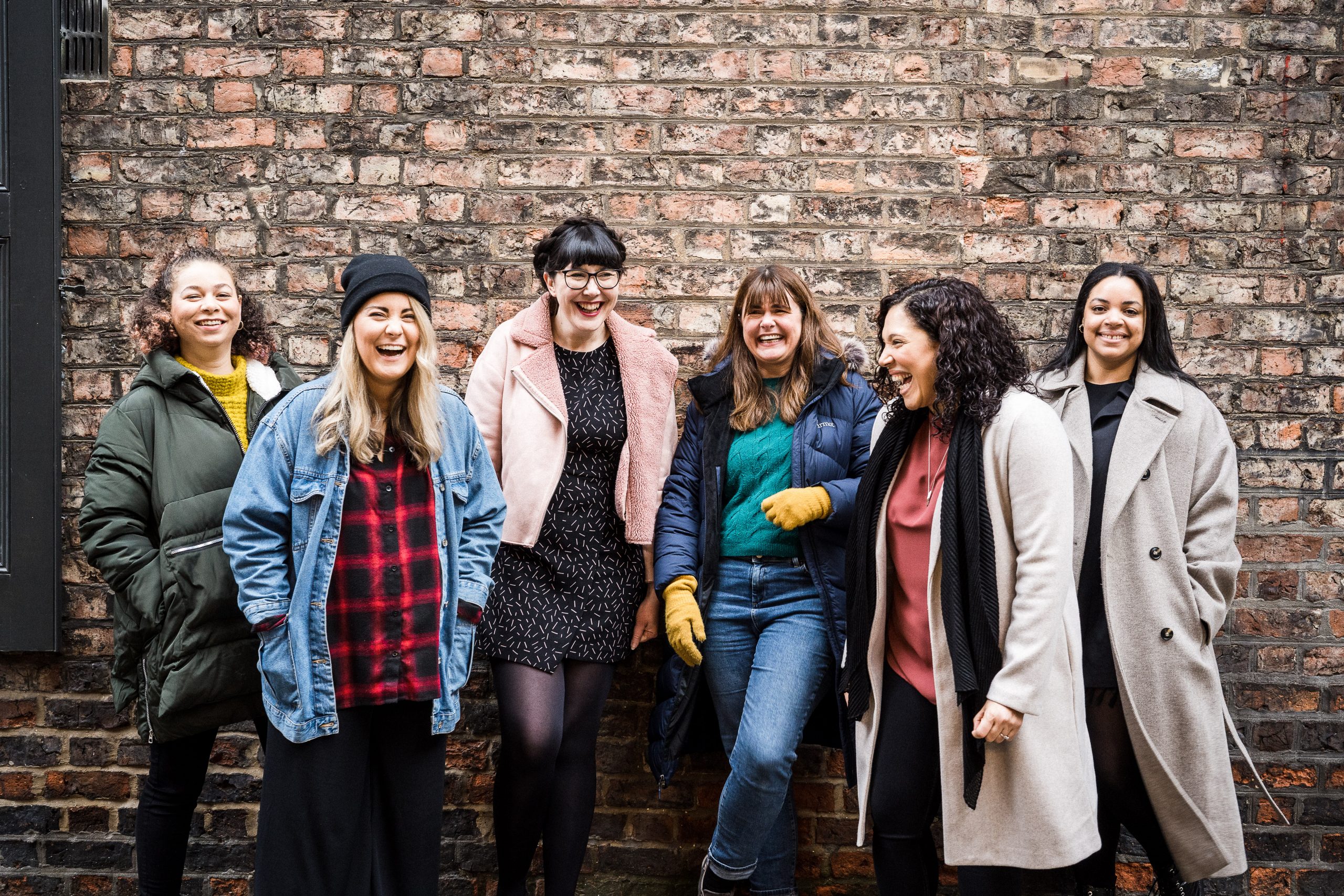 Alt text: The Pregnant Then Screwed team laughing together in front of a brick wall