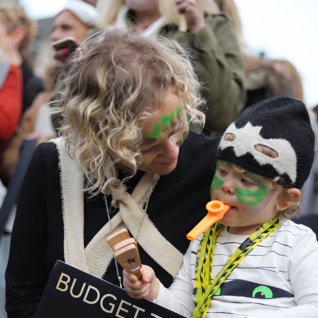 Image description: Woman with her baby at the March of the Mummies Protest 2017 with face paints on holding a placard