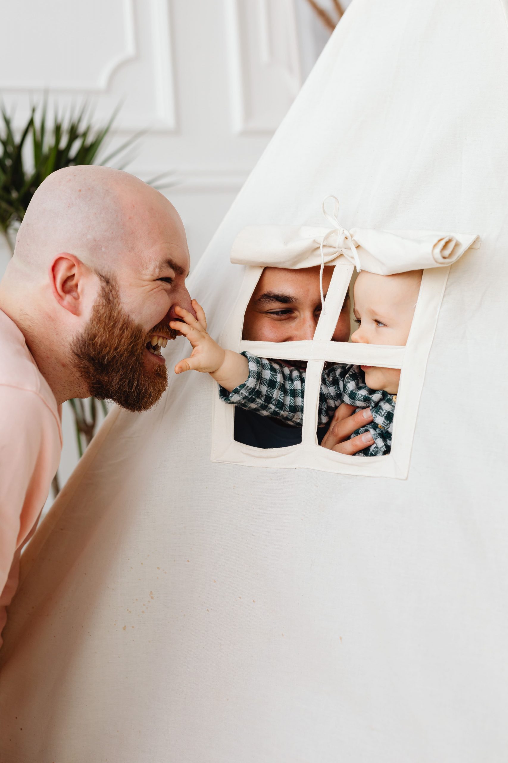 Image description: Two fathers playing with their baby in a tent, all laughing