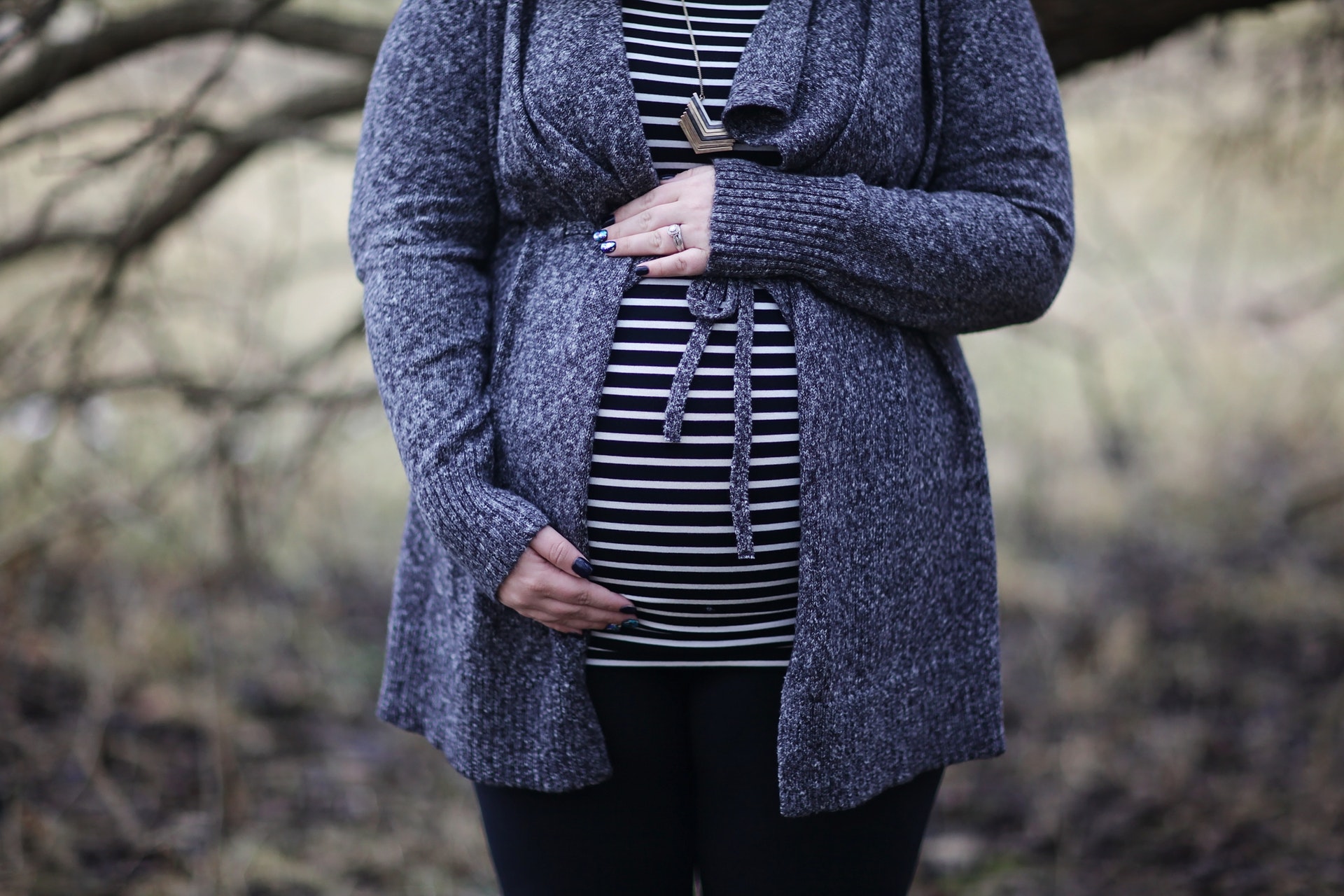 A woman's pregnant belly in a striped shirt and grey cardigan